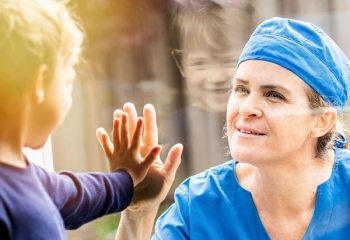 Healthcare working touching hands with small child through glass