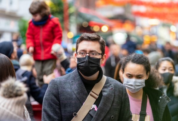 Photograph of two people walking against crowd with face masks on