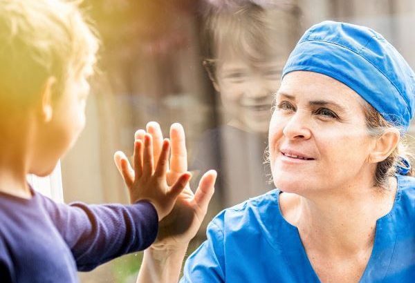 Healthcare working touching hands with small child through glass