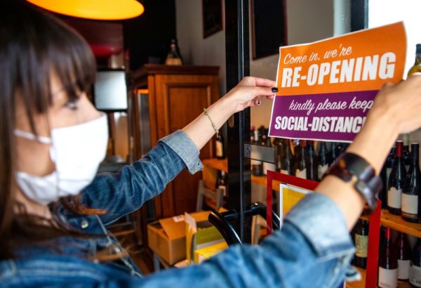 Woman with mask posting sign on business door
